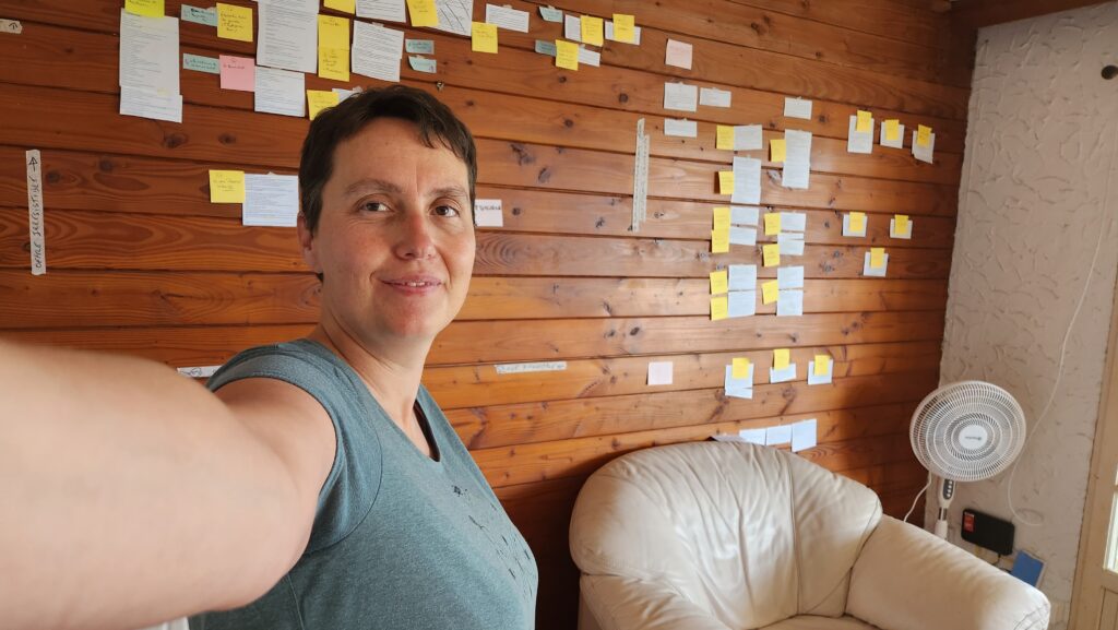 Agnes V. souriante devant un mur rempli de post-it, illustrant la persévérance et la structuration d’un projet ambitieux, malgré les doutes et les obstacles.