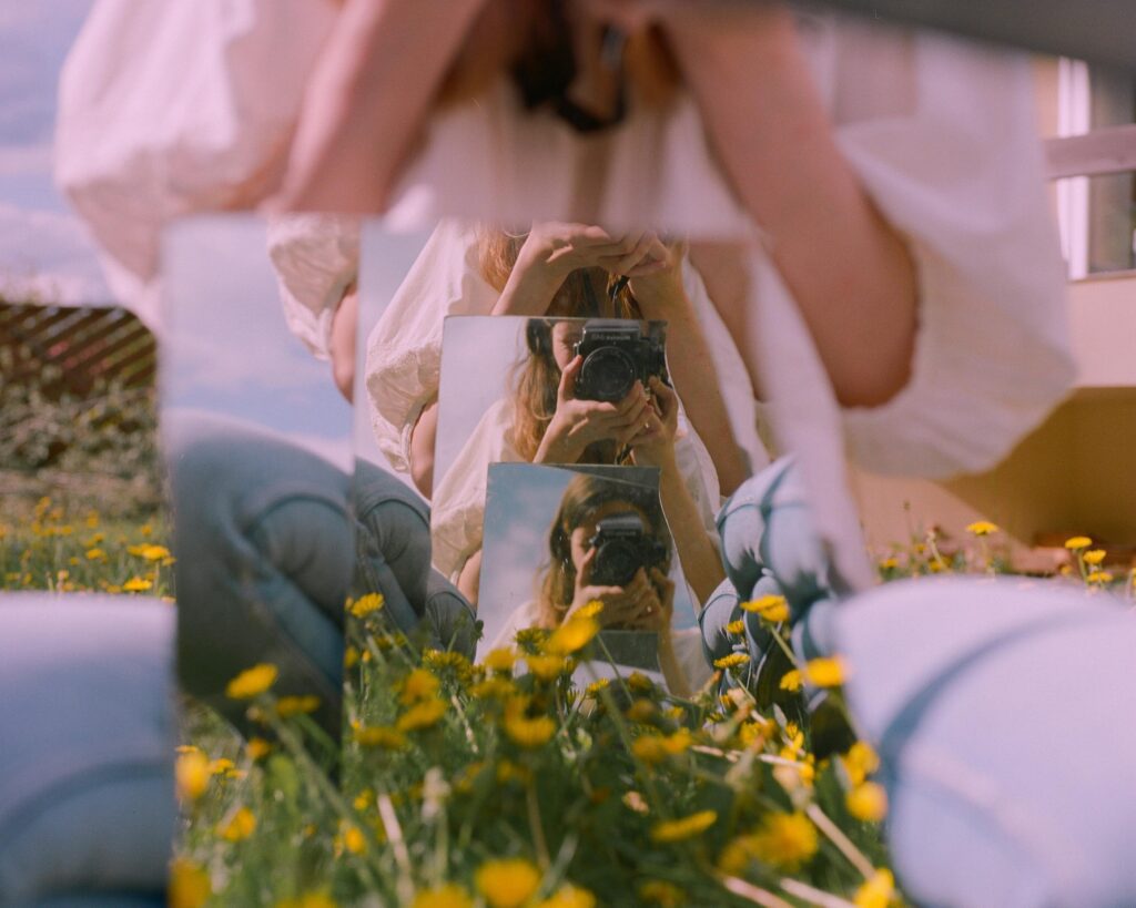 Reflet d’une femme photographe dans plusieurs miroirs posés dans un champ de fleurs, illustrant la multiplicité des regards sur la puissance féminine.