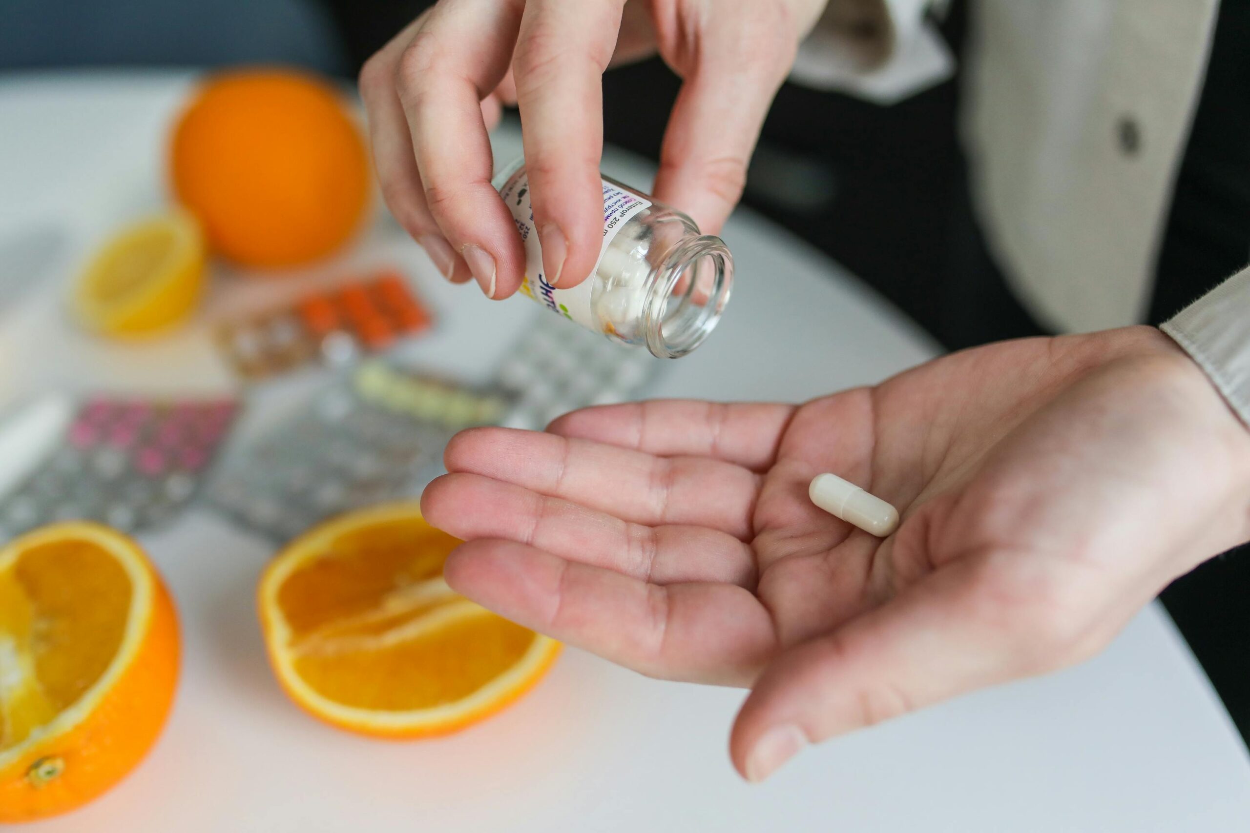Femme prenant une gélule de vitamine dans la main, avec des oranges coupées en arrière-plan